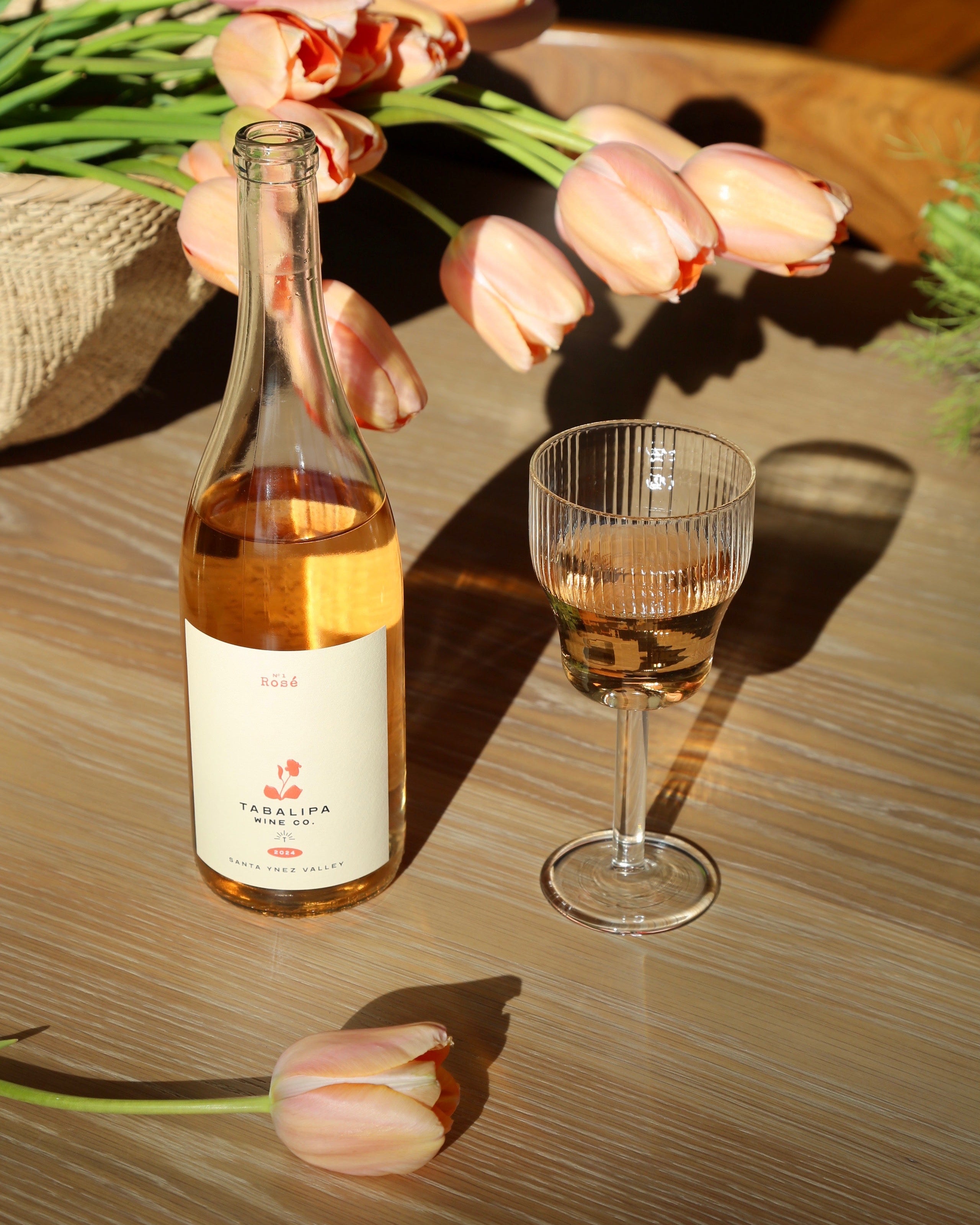 Tabalipa Nº1 Rosé wine bottle in outdoor vineyard setting with glass or rosé to the right of the bottle.