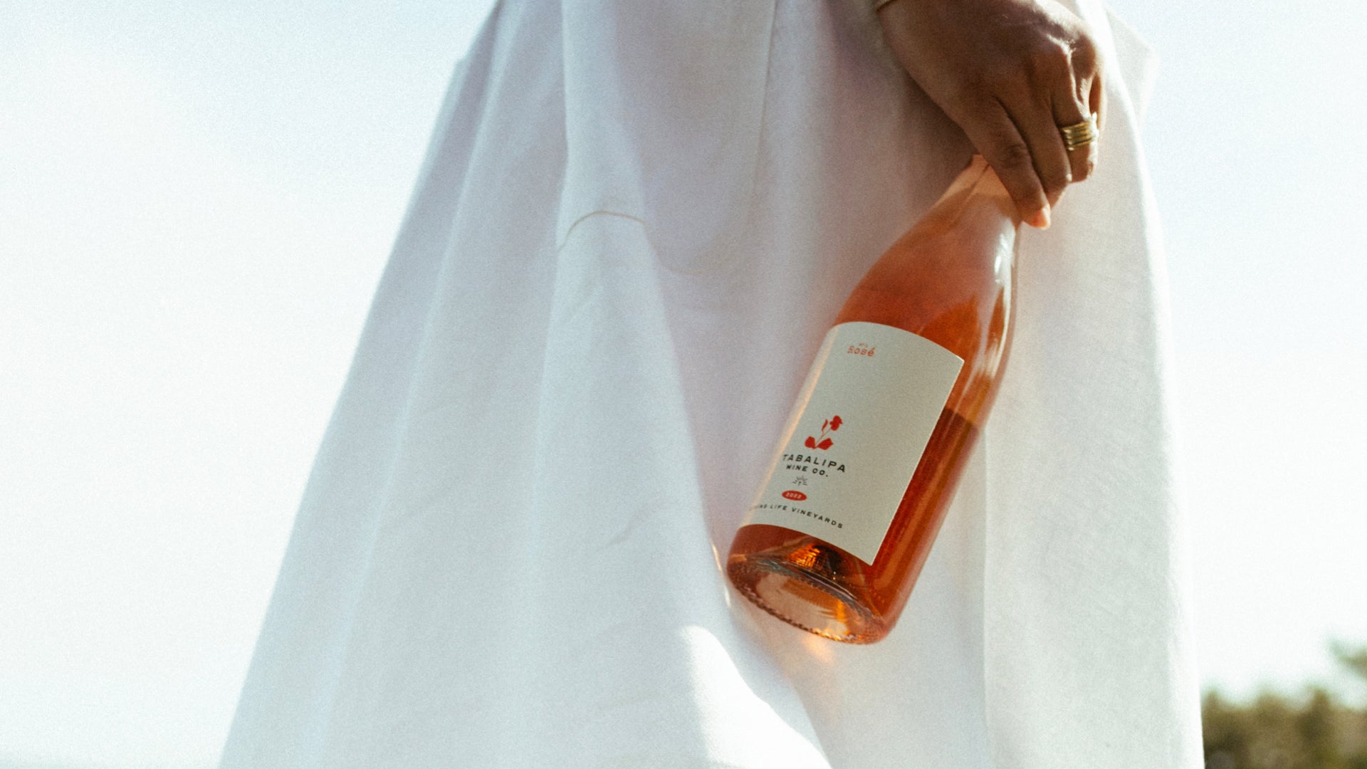 Woman wearing white dress holding a bottle of rosé wine with a blurred background
