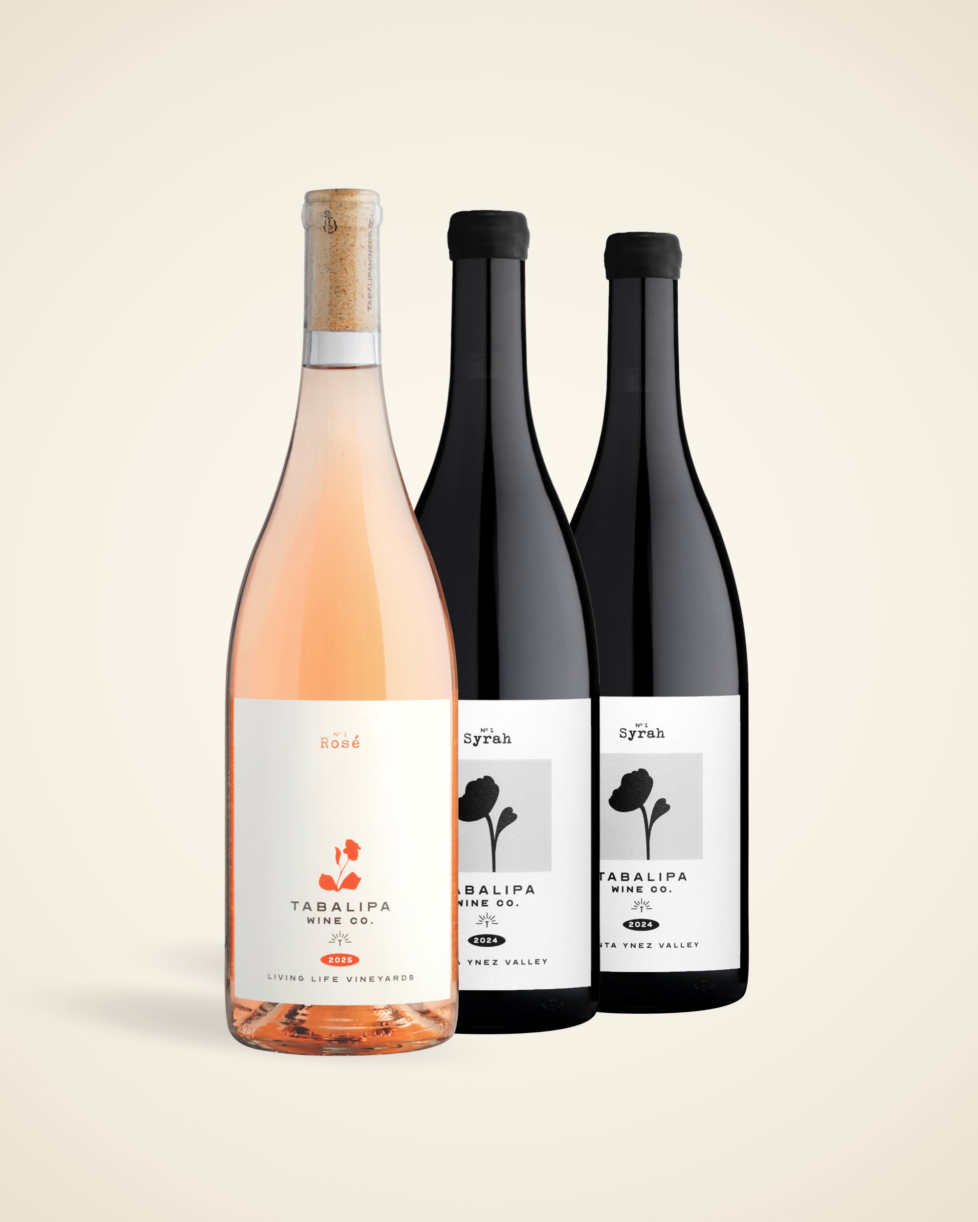 Three wine bottles from Tabalipa Vineyard arranged together on a light beige background: a rose wine bottle in front with a cork stopper and pale pink liquid, flanked by two dark red wine bottles with black caps and white labels.