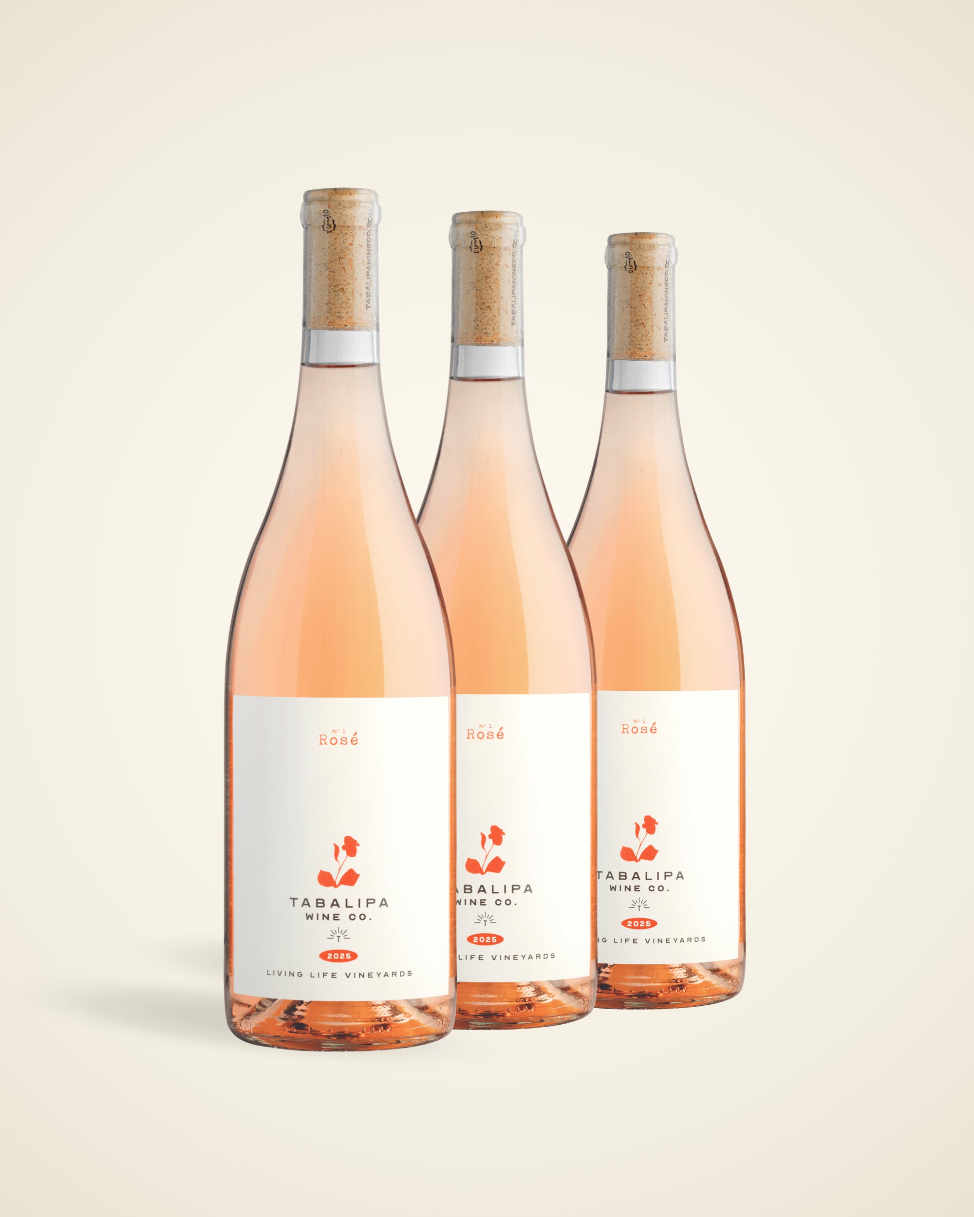 Three bottles of Tabalipa Rosé wine arranged together on a light beige background. The bottles are filled with pale pink rosé wine, have cork stoppers, and white labels with orange and black text.