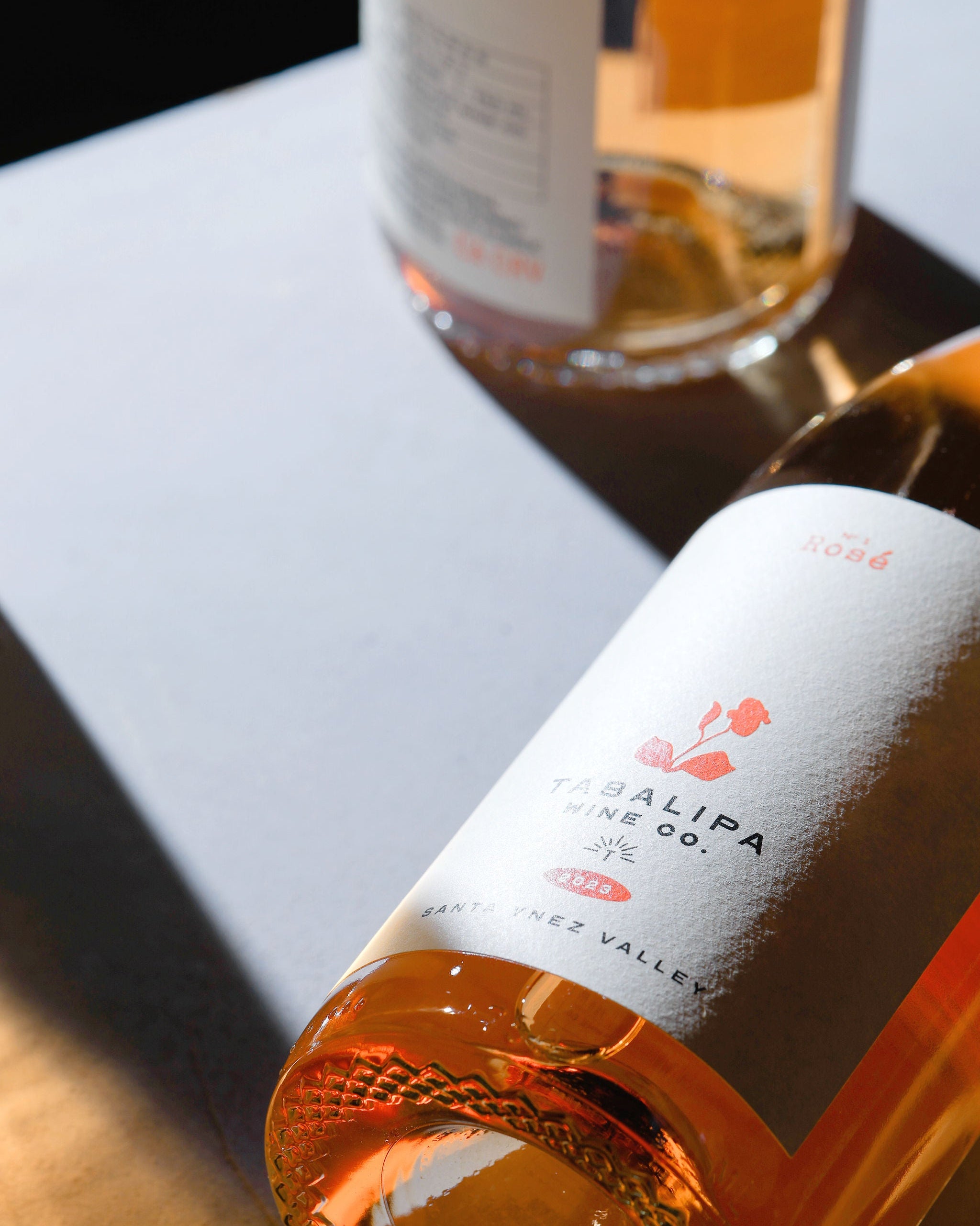 Two bottles of rosé one laying down on a white table and the other standing up with moody contrast lighting.